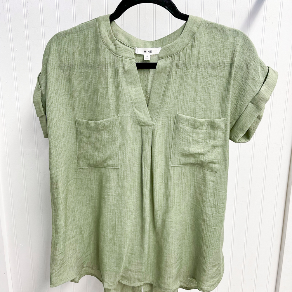 Easy To Style light olive Woven Top, woven women's short sleeve top with v-neck with detail. double front pocket detail. back button detail going down the center. 