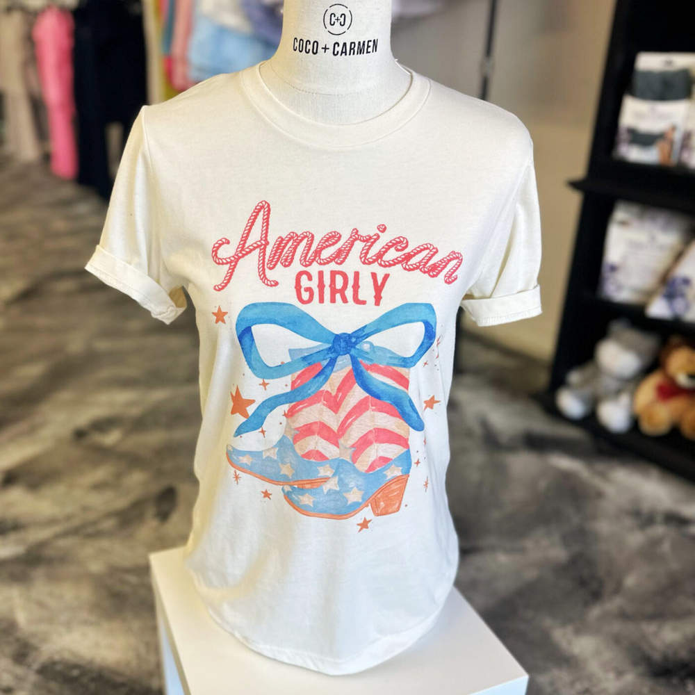 4th of july t shirt, american girly, pair of cowboy boots with stars and stripes like the american flag with a big blue bow on top and stars floating around the boots