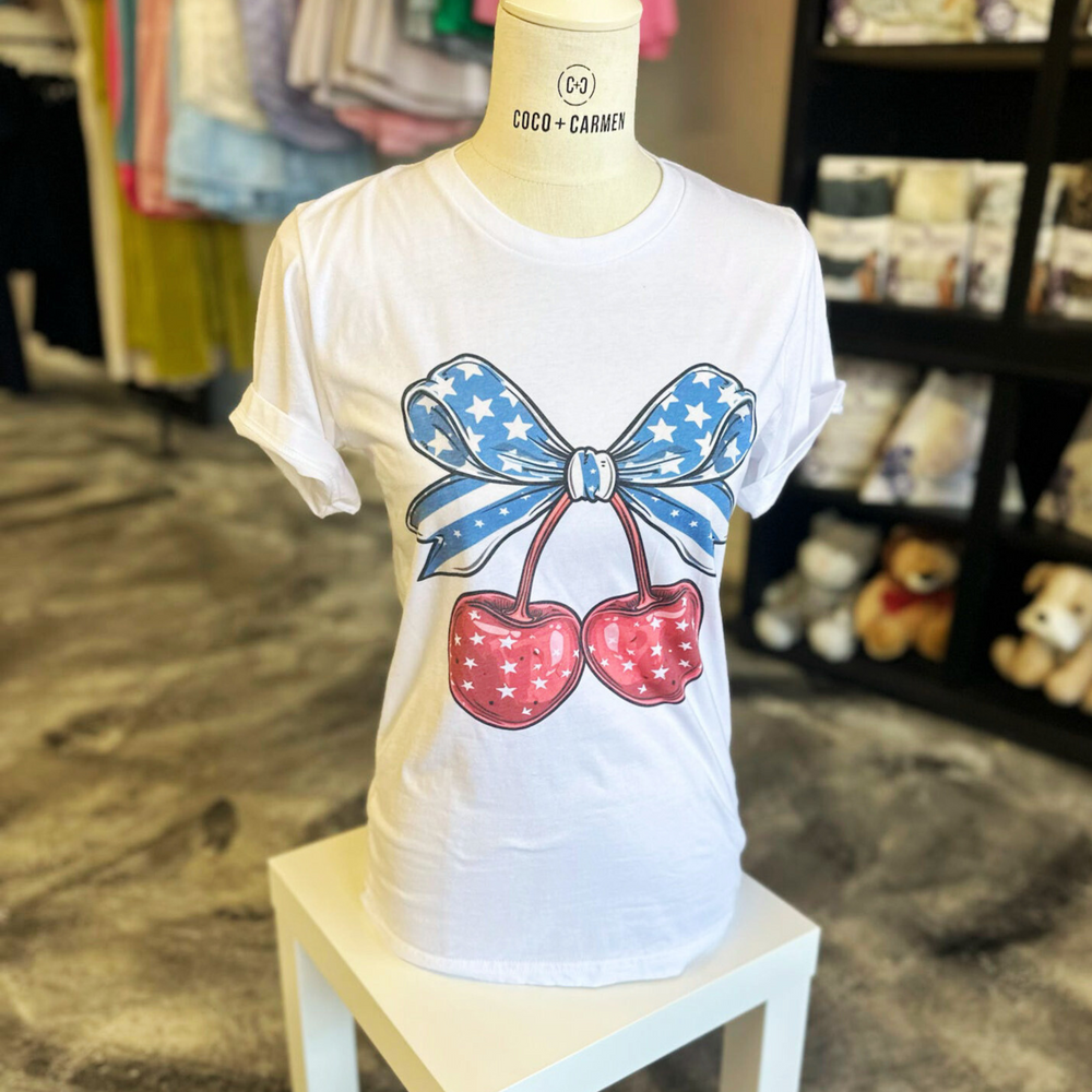 4th of july t shirt, white t shirt with a big pair of cherries on the front, red cherries with white stars, big blue bow on top of the cherries with navy and white stripes and stars