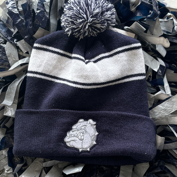 Navy beanie with white stripe and navy and white puff topper and bulldog patch on the front.