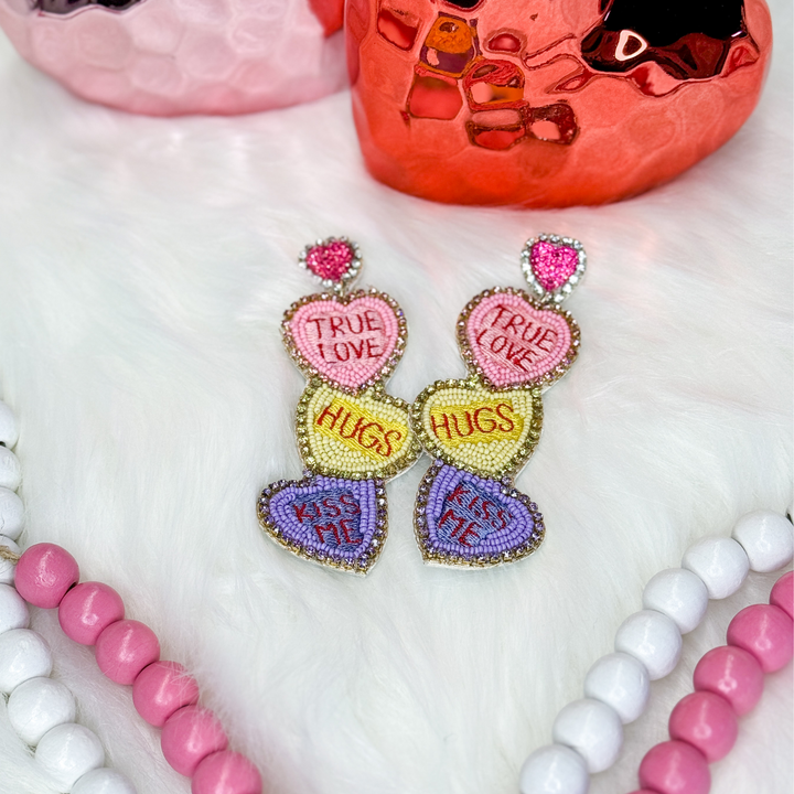 Valentine's Day beaded earrings featuring multi-colored conversation hearts. Light pink with "true love", yellow with "hugs", purple with "kiss me"