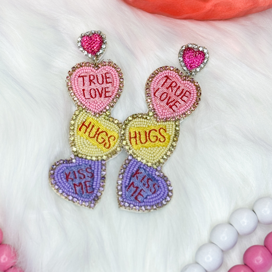 Valentine's Day beaded earrings featuring multi-colored conversation hearts. Light pink with "true love", yellow with "hugs", purple with "kiss me"