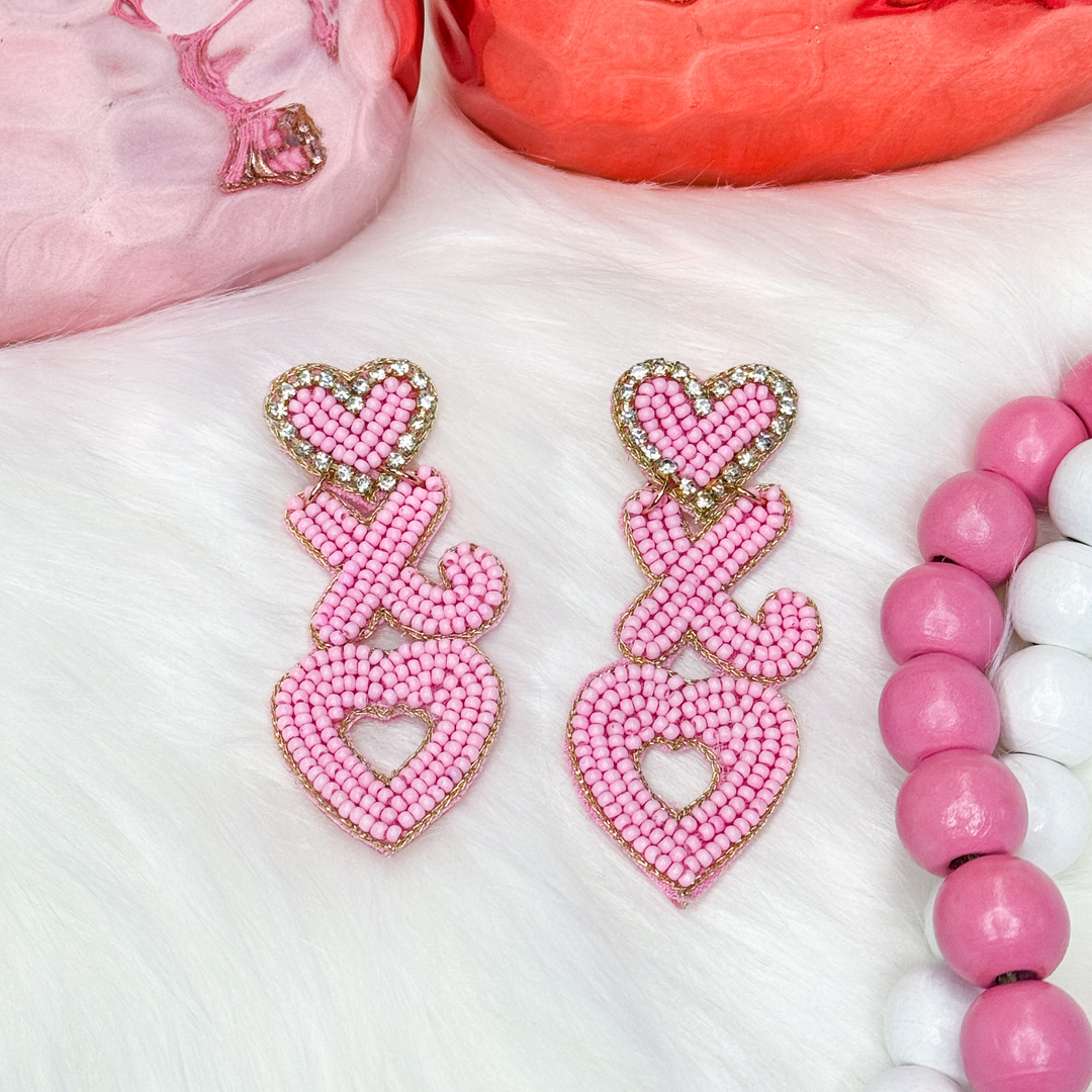 light pink valentine's day earrings. small heart on the top, followed by an x and an o vertically. small heart is outlined in gold.