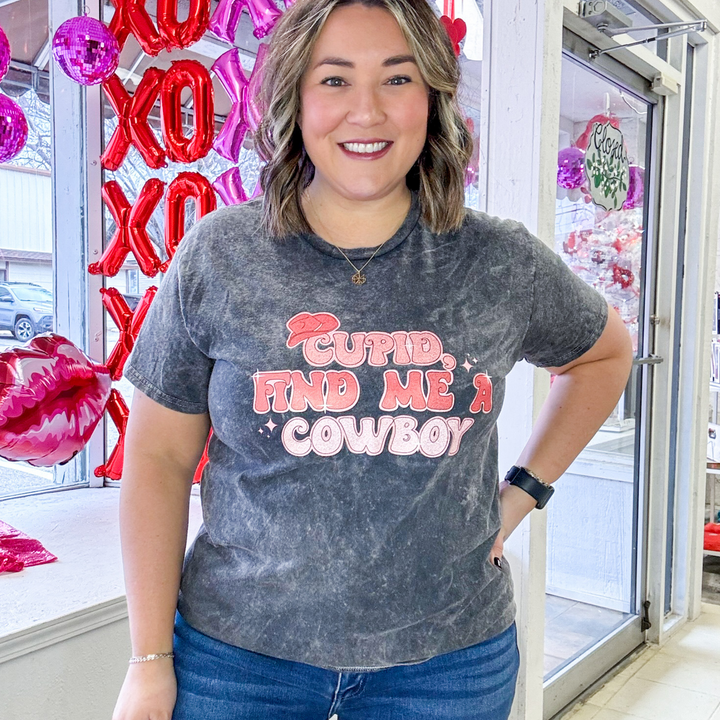 light washed gray tshirt with bubble font that says "cupid find me a cowboy" in different shades of pink and small cowboy hat on the word cupid