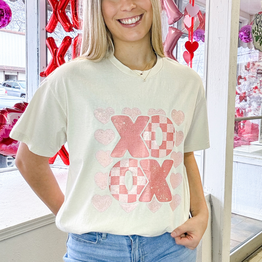 cream colored valentines graphic t shirt with xo,ox, shades of pink, the o's have a checkered pattern to them