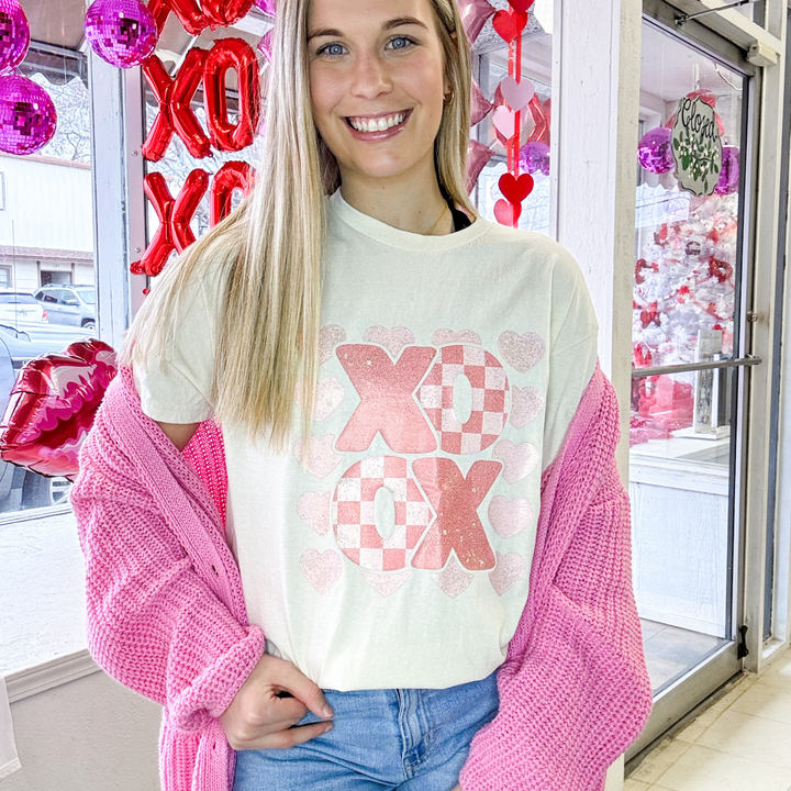 cream colored valentines graphic t shirt with xo,ox, shades of pink, the o's have a checkered pattern to them