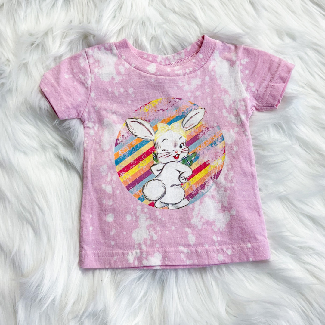 easter tee, kids tee, bubble gum pink with white bleach spot, rainbow stripe circle with retro bunny winking in the middle of the circle