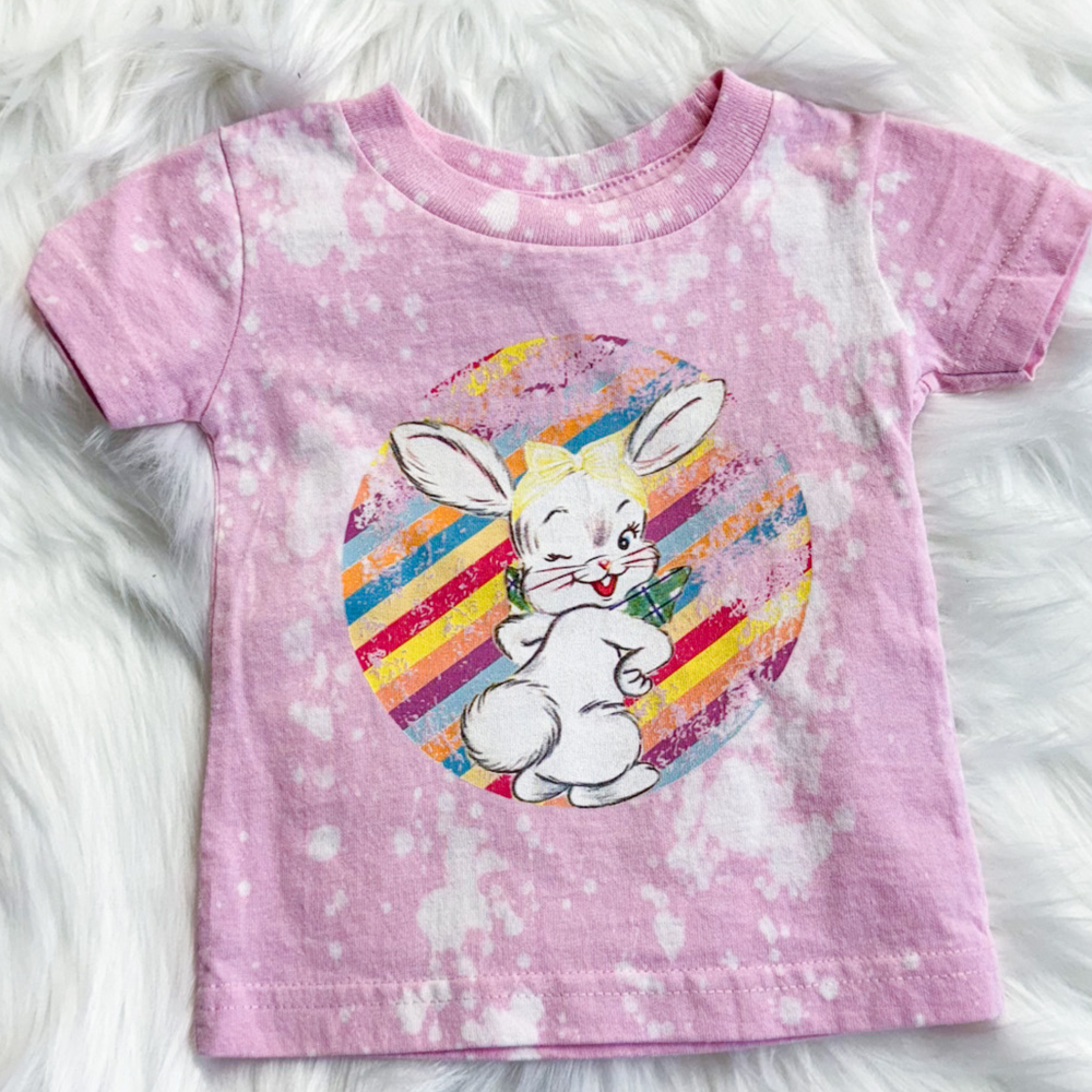 easter tee, kids tee, bubble gum pink with white bleach spot, rainbow stripe circle with retro bunny winking in the middle of the circle
