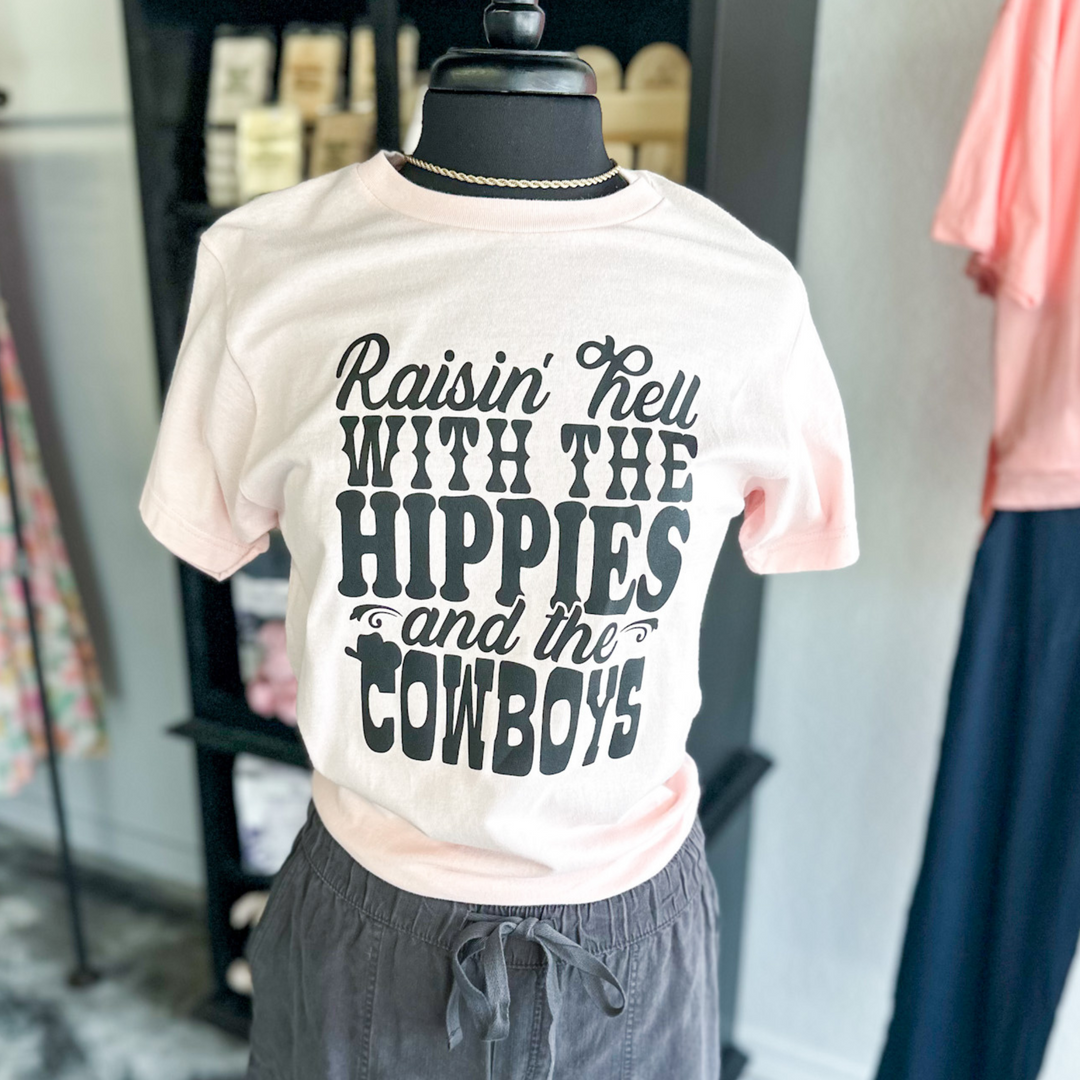 light pink short sleeve, says Raisin' hell with the hippies and the cowboys in black