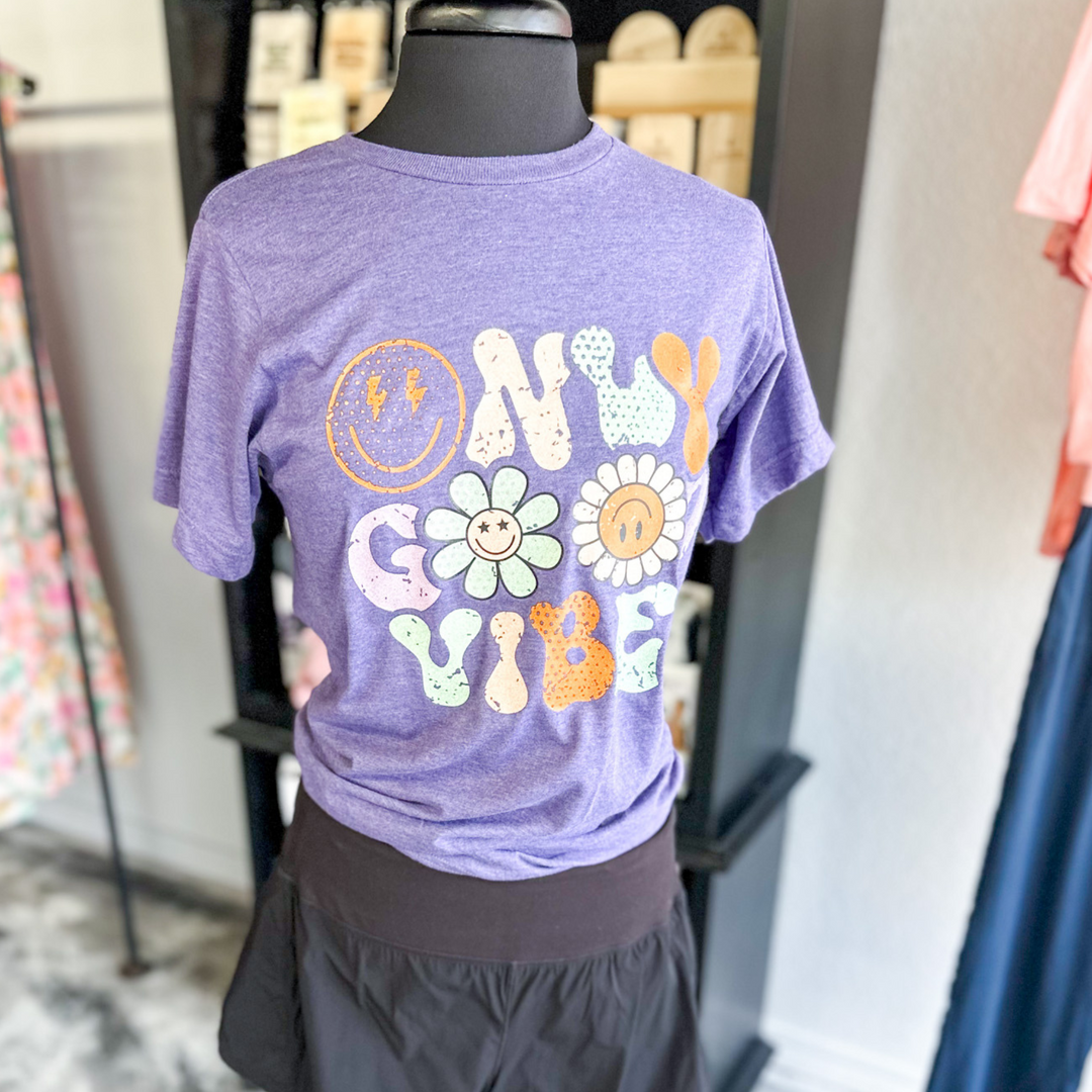 purple short sleeve shirt, says only good vibes with mismatch colors on letters, orange, light blue, light purple, flowers for o in good, smiley face for o in only