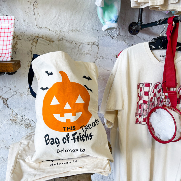halloween trick or treat bag, orange jack o lantern. cute black graphics under the pumpkin that says this bag of tricks (crossed out) treat belongs to blank. bat details.