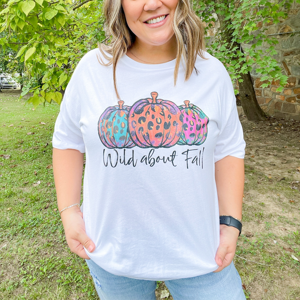 wild about fall fall graphic tee, white round neck tee shirt with 3 pumpkins with multi color leopard on them, under the pumpkins in a black script font it says wild about fall. 